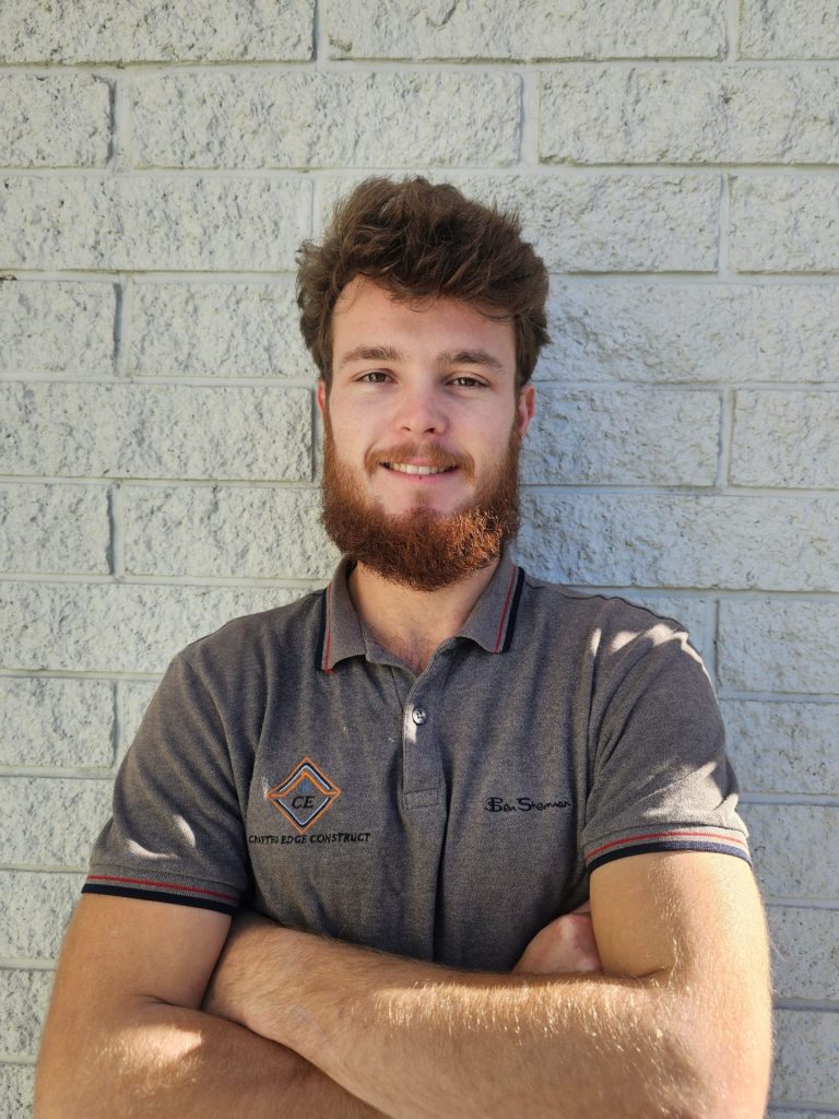 Crafted Edge Construct professional builder standing with arms crossed against a white brick wall.