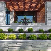 Custom outdoor patio with a timber pergola, stone columns and professionally landscaped garden beds.