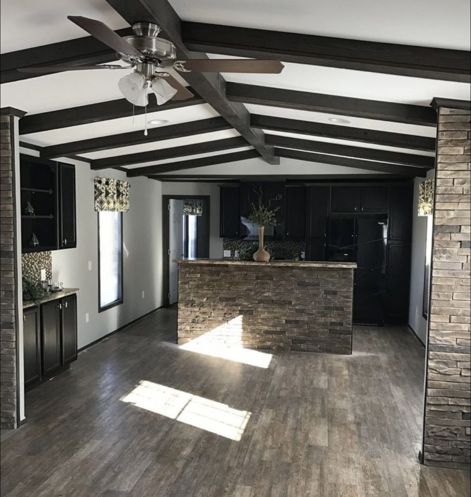 Modern open-plan kitchen renovation with exposed ceiling beams, dark cabinetry, stone feature walls and timber-look flooring.